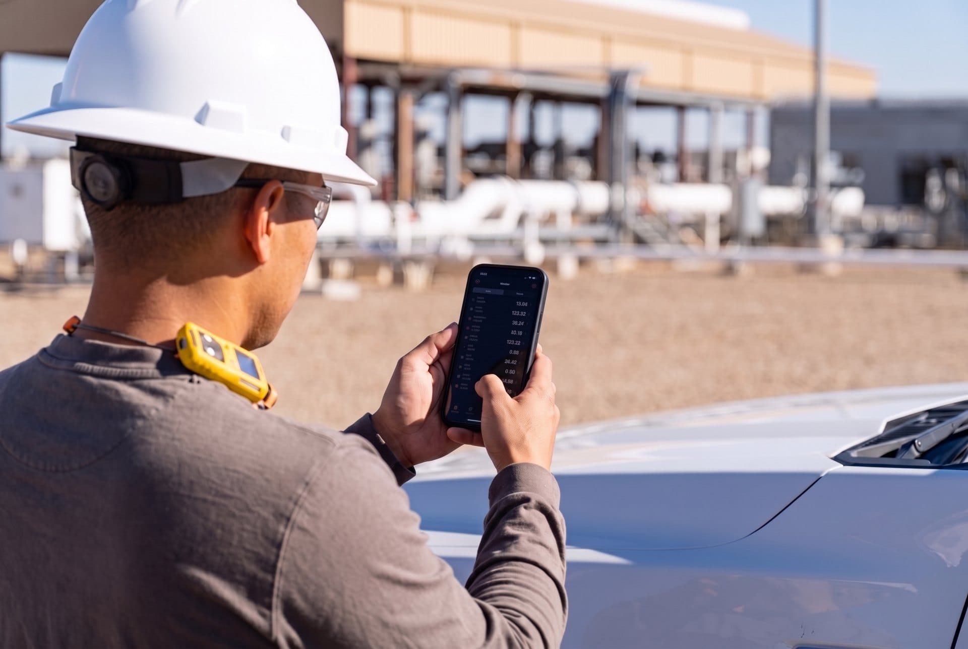Over-the-shoulder view of an operator using a phone at a truck hood with compressor equipment behind him